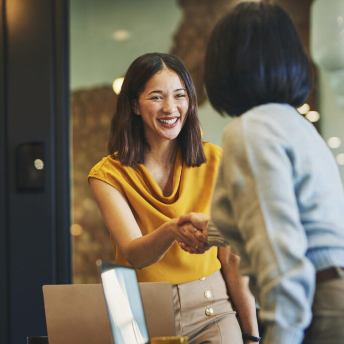 Businesswoman shaking hands with client and smiling cheerfully in meeting room