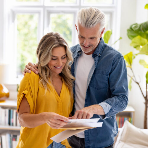 Happy Caucasian couple checking their mail at home and smiling - domestic life concepts