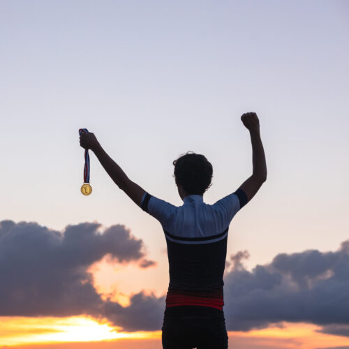 Silhouette of an athlete celebrating the gold medal against a sunset sky adorned with golden clouds in the background. Ideal for conveying the spirit of success in sporting events.